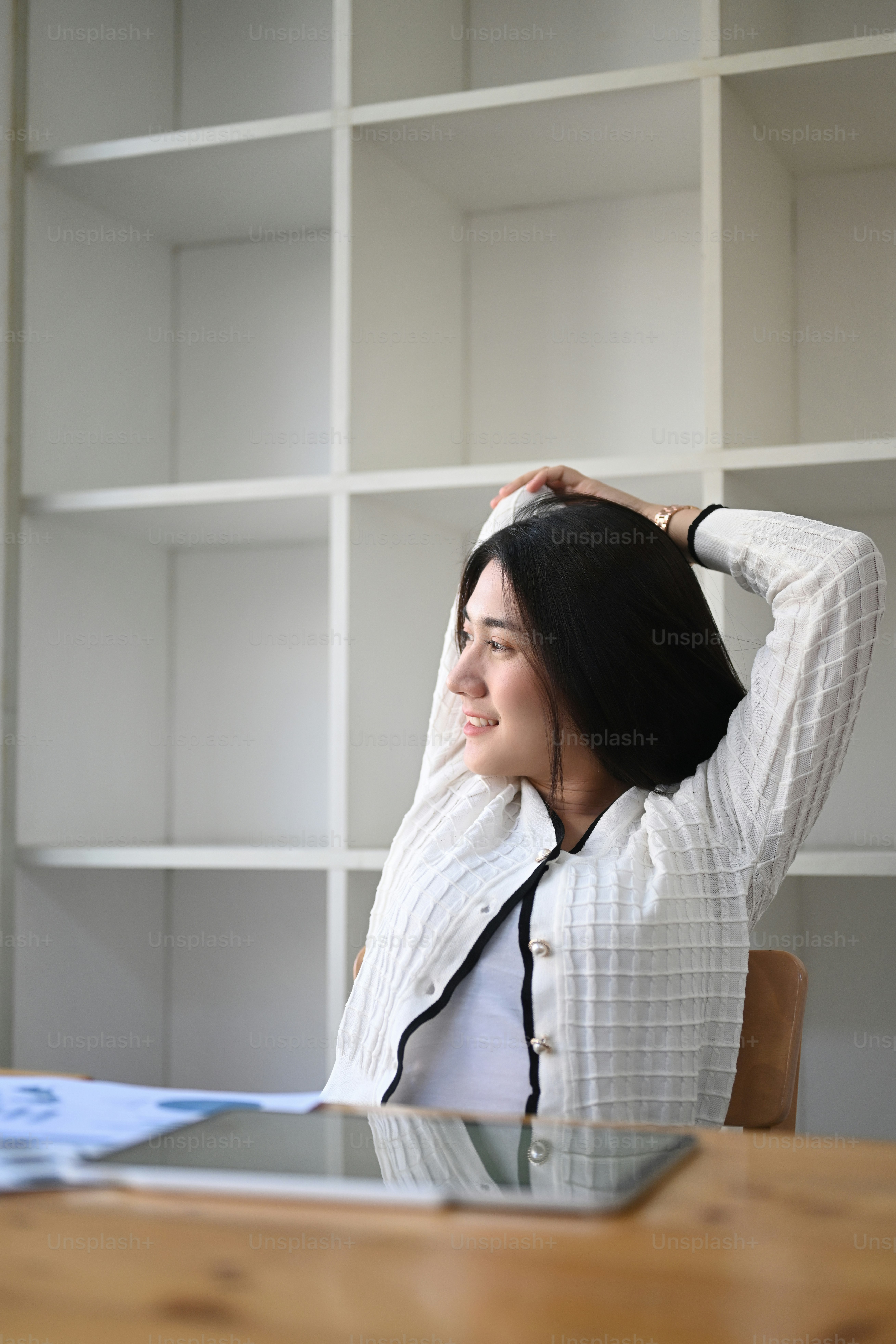 Retrato de empresária sentada no espaço de trabalho e esticando os braços acima da cabeça e olhando pela janela com um sorriso.