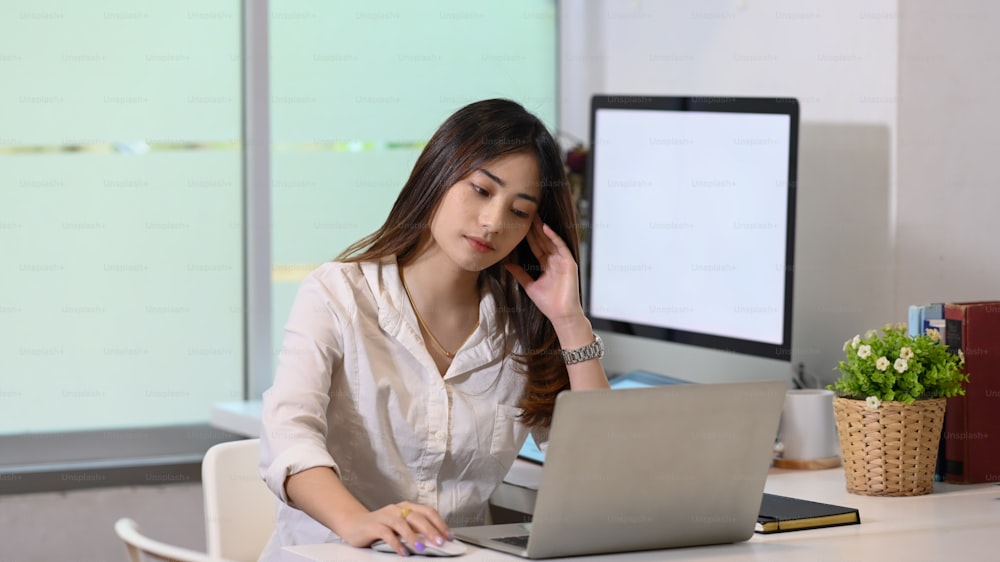 Thoughtful female employee looking at computer screen and thinking of problem solution.