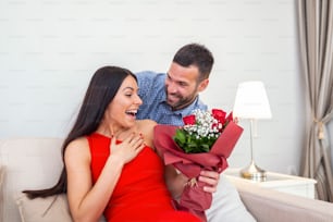 Aufgeregte junge Frau, die unerwarteten Strauß roter Rosen vom Ehemann zu Hause erhält, liebevoller großzügiger Freund, der eine romantische Überraschung für eine attraktive Freundin am Valentinstag macht