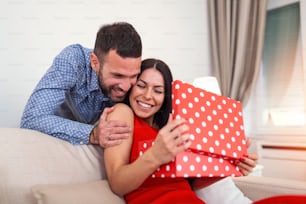 Young couple at home holding a present. Man suprising his wife with gift box on Valentines day.