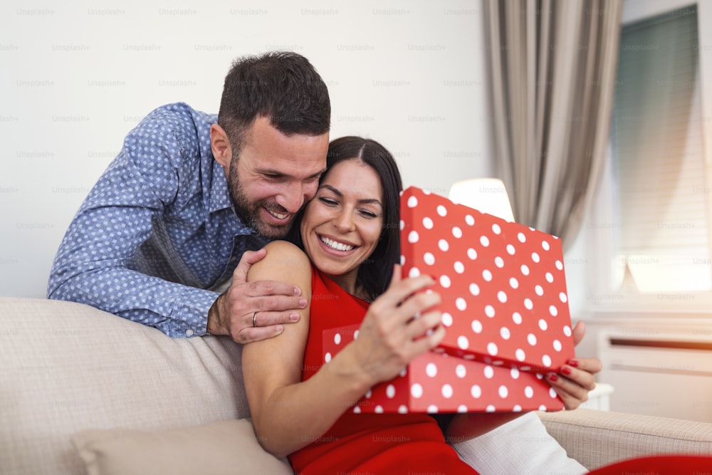 Young couple at home holding a present. Man suprising his wife with gift box on Valentines day.