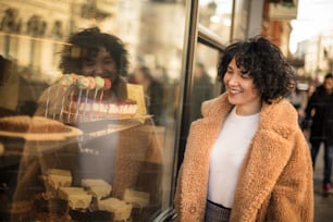Smiling woman stands next to a pastry shop window.