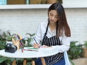 庭のコーヒーテーブルに色鉛筆でエプロンを描いた女性アーティストの肖像画