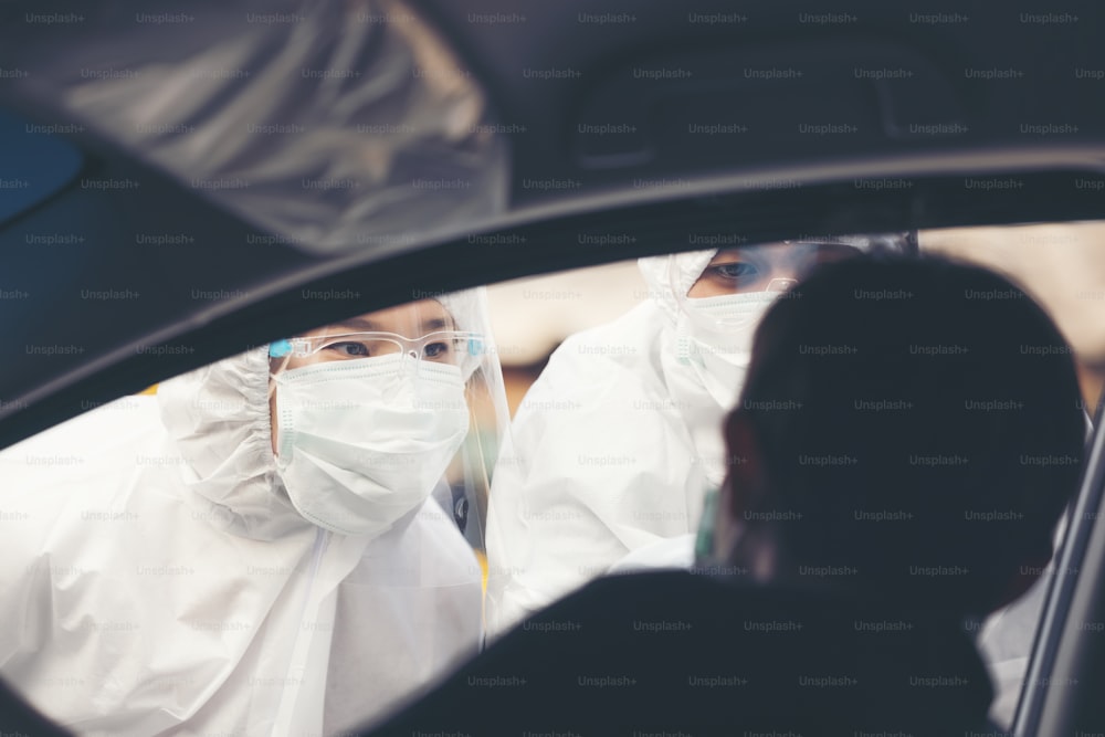 Mujer asiática conduce a través de las pruebas de Covid-19 con personal médico de EPP, prueba de COVID temporal mientras registra los automóviles