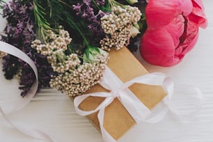 Feliz dia das mães e conceito de Dia dos Namorados. Caixa de presente artesanal elegante e buquê com flores de peônia, lilás e rosas no fundo de madeira branca de perto. Vista superior