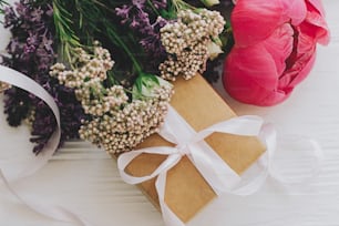 Happy mothers day and valentines day concept. Stylish craft gift box and bouquet with peony, lilac and roses flowers on white wooden background close up. Top view