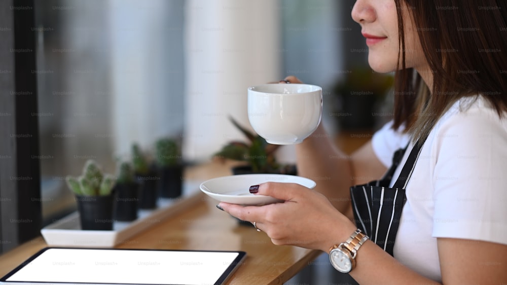 Vista ravvicinata dell'imprenditrice di una caffetteria che tiene in mano una tazza di caffè caldo e prova da sola.