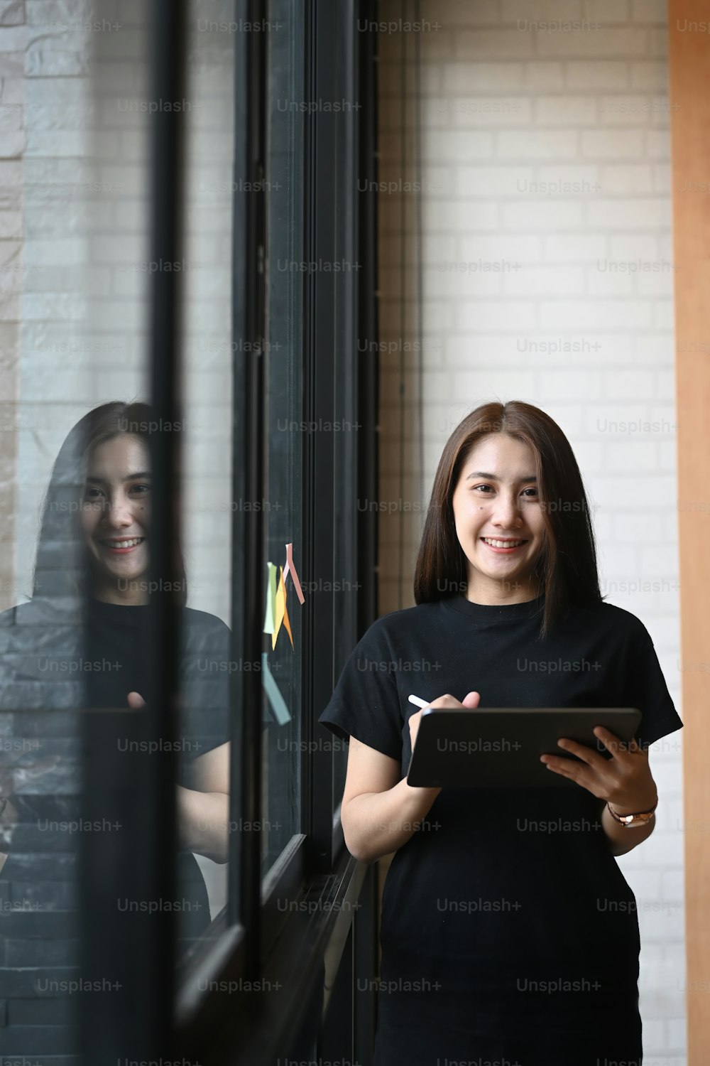 Retrato da jovem empresária segurando o tablet digital e sorrindo para a câmera enquanto estava perto da janela do escritório.