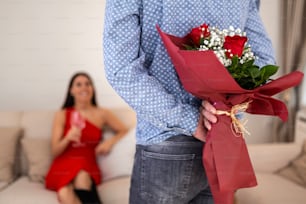 Happy woman looking at her boyfriend holding bouquet of roses behind his back. Handsome man holding flowers behind his back to surprise his girlfriend, romantic happy couples on Valentines day