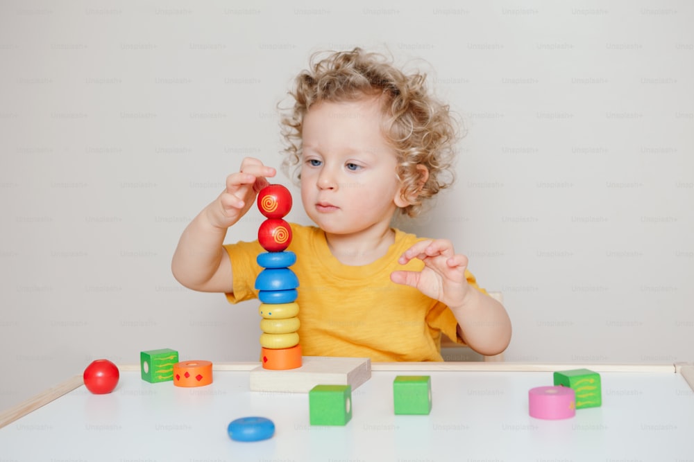 Lindo bebé pequeño jugando con bloques de apilamiento de pirámides de juguete de aprendizaje en casa o jardín de infantes. Educación en la primera infancia. Actividad divertida de desarrollo del cerebro de la mano de los niños para niños en edad preescolar.