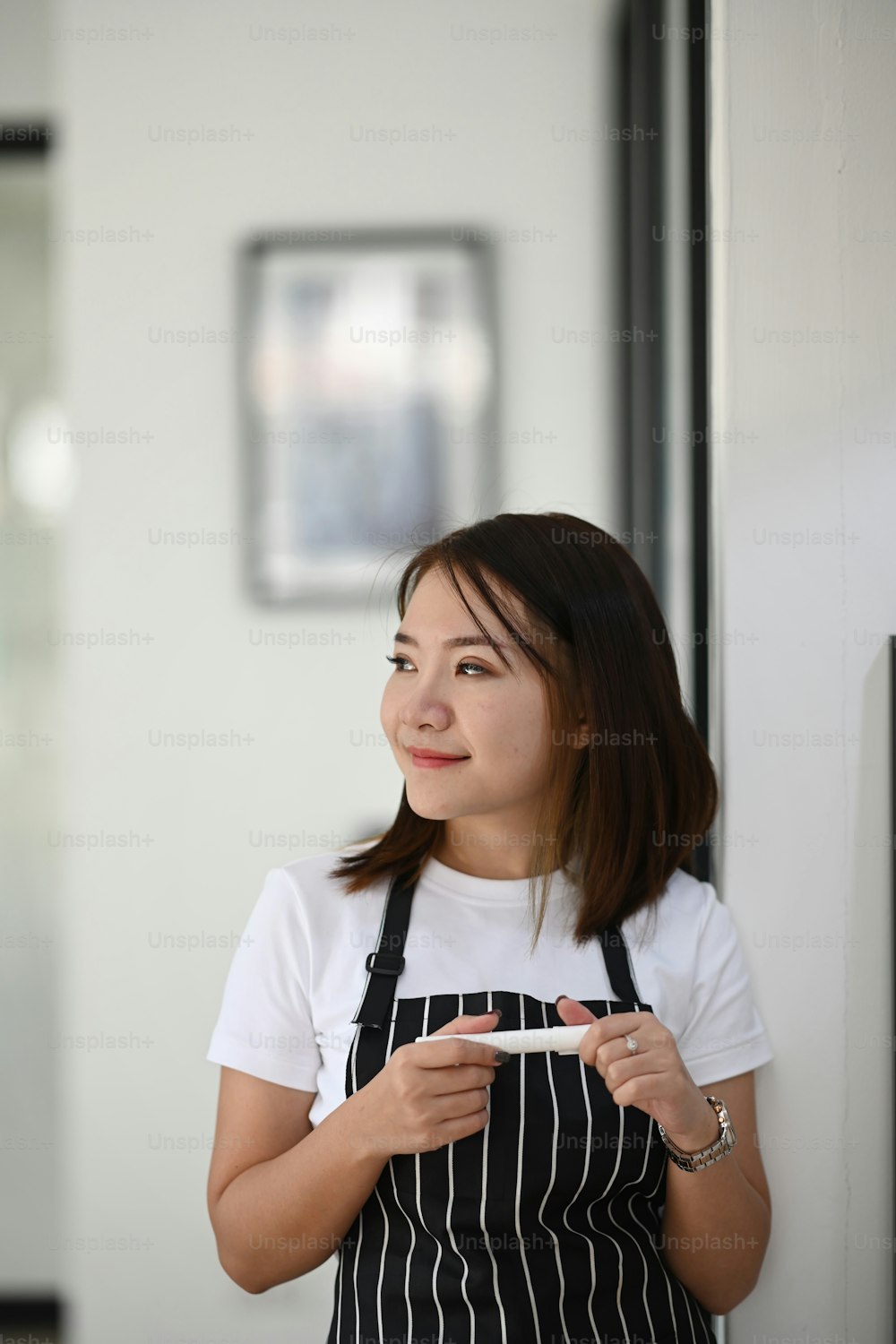 Portrait of female owner in an apron standing and looking through out of window at her coffee shop.