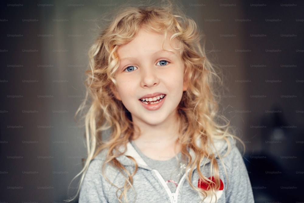 Closeup portrait of beautiful smiling Caucasian blonde girl with long messy hair. Pretty real girl child with natural emotions. Happy authentic childhood lifestyle. Missing lost milk tooth.