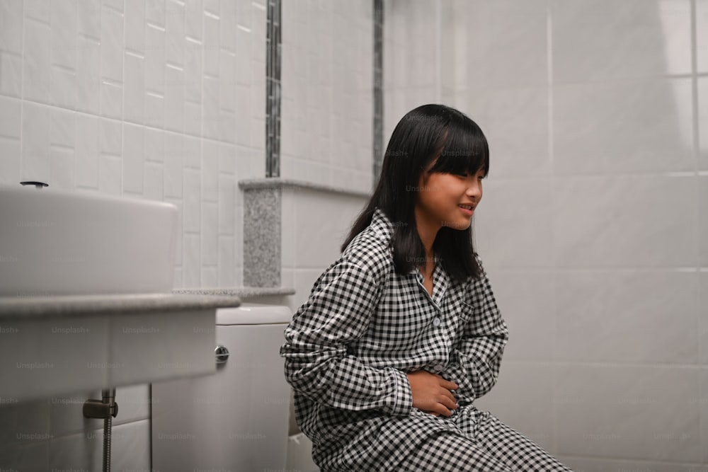 Asian girl sitting in toilet at home and suffering from stomachache.