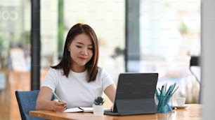 편안한 직장에서 정보를 확인하기 위해 태블릿 컴퓨터에서 일하는 젊은 여성 프리랜서.