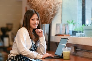 Ritratto di donna proprietaria di una piccola impresa seduta all'interno della sua caffetteria e utilizzando la tavoletta digitale.