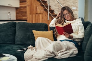 Foto de una mujer joven leyendo un libro mientras se relaja en casa