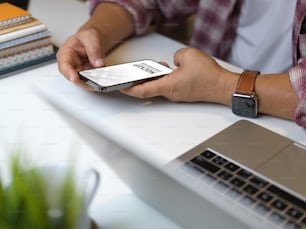 Vista laterale della mano dell'uomo d'affari che utilizza lo smartphone sul tavolo da lavoro con forniture per ufficio nella stanza dell'ufficio