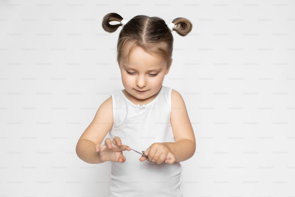 爪切りを使用して手に爪をトリミングする小さな愛らしい子供の女の子の肖像画を接写します。健康的な衛生手順、子供のネイルケアのコンセプト。