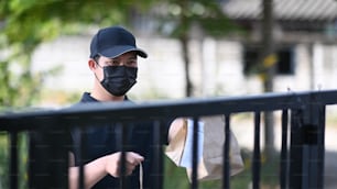 Deliver man in protective mask  holding paper bag with food and waiting customer at doorway. Food delivery service.