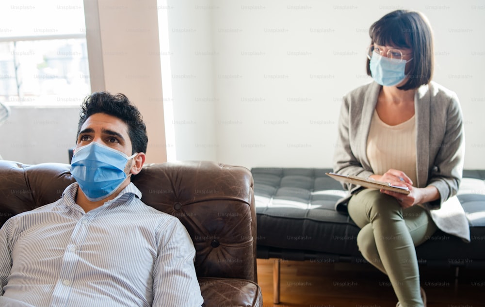 Portrait of a psychologist talking with her patient and taking notes while he's lying on couch during a therapy session. New normal lifestyle. Psychology and mental health concept.