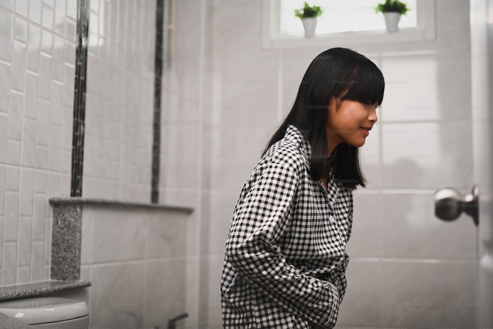 Asian girl suffering from stomachache and standing in toilet at home.