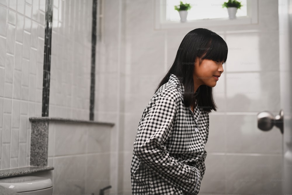 Menina asiática que sofre de dor de estômago e em pé no banheiro em casa.
