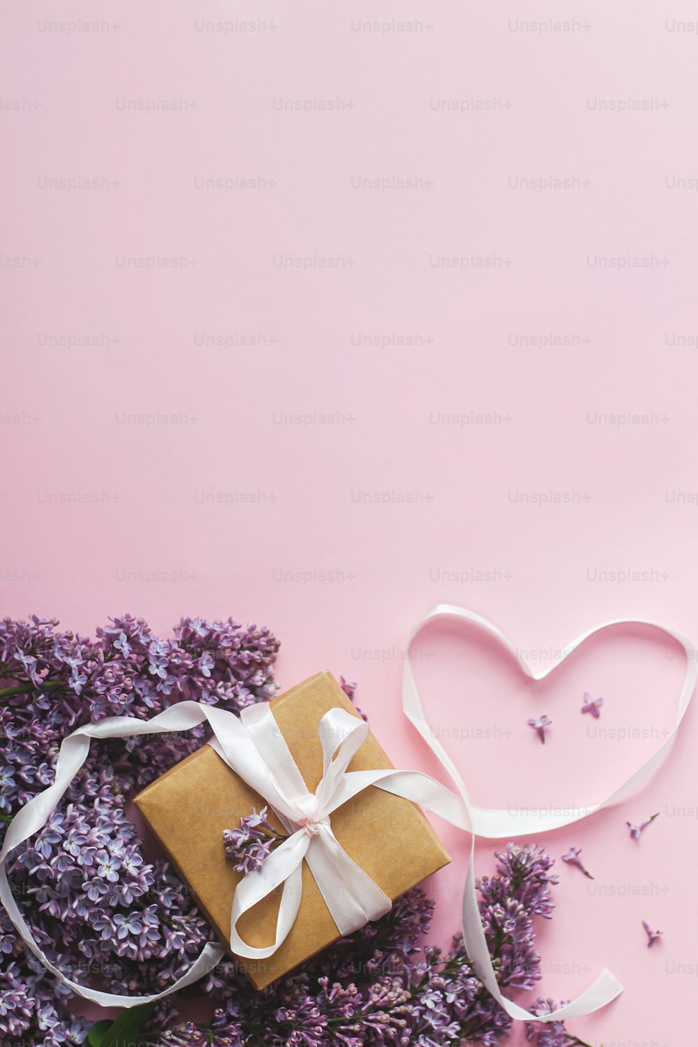 Fliederblumen, Geschenkbox und Herzband auf rosa Papier, flach gelegt mit Kopierraum. Stilvolle Blumengrußkarte. Alles Gute zum Valentinstag und Muttertagskonzept. Lila Fliederstrauß und Bastelgeschenk