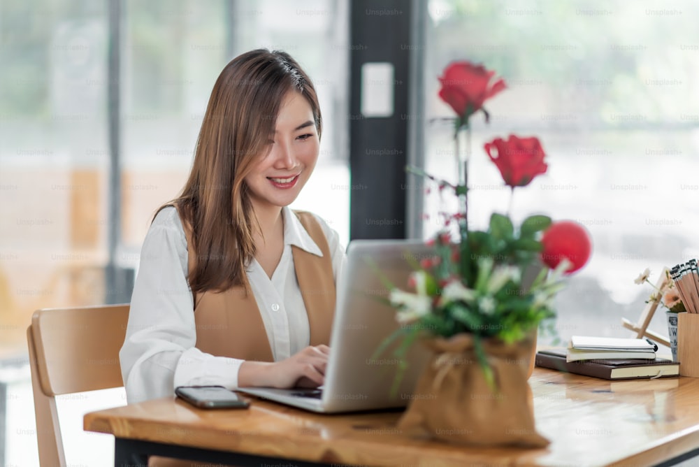 Beautiful young asian woman sitting at coffee shop using laptop. Happy young businesswoman sitting at table in cafe with tab top computer.