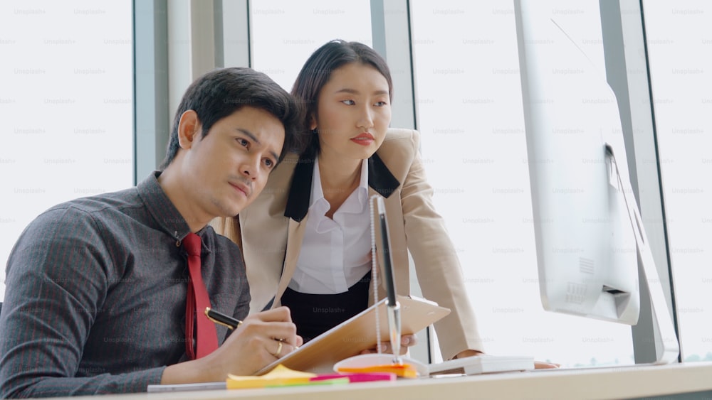 Two business people talk project strategy at office meeting room. Businessman discuss project planning with colleague at modern workplace while having conversation and advice on financial data report.