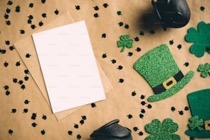 Happy St Patrickâs day concept. Flat lay composition with blank greeting card mockup, Irish elf hats, pots of gold, shamrock clover leaves on craft paper. Vintage, retro style.
