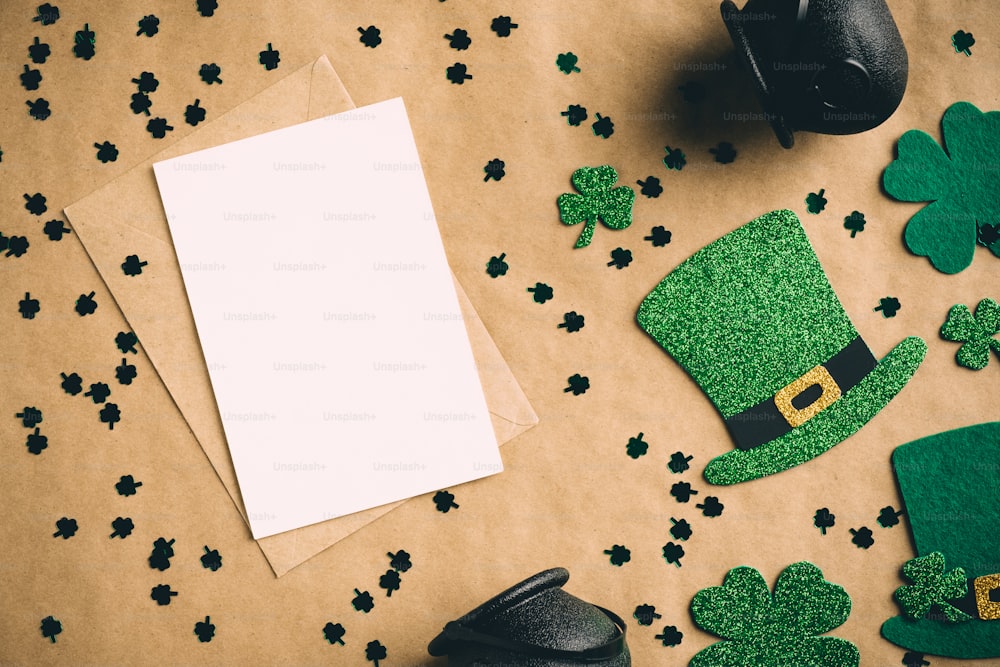 Feliz concepto del día de San Patricio. Composición plana con maqueta de tarjeta de felicitación en blanco, sombreros de elfo irlandés, ollas de oro, hojas de trébol de trébol en papel artesanal. Vintage, estilo retro.