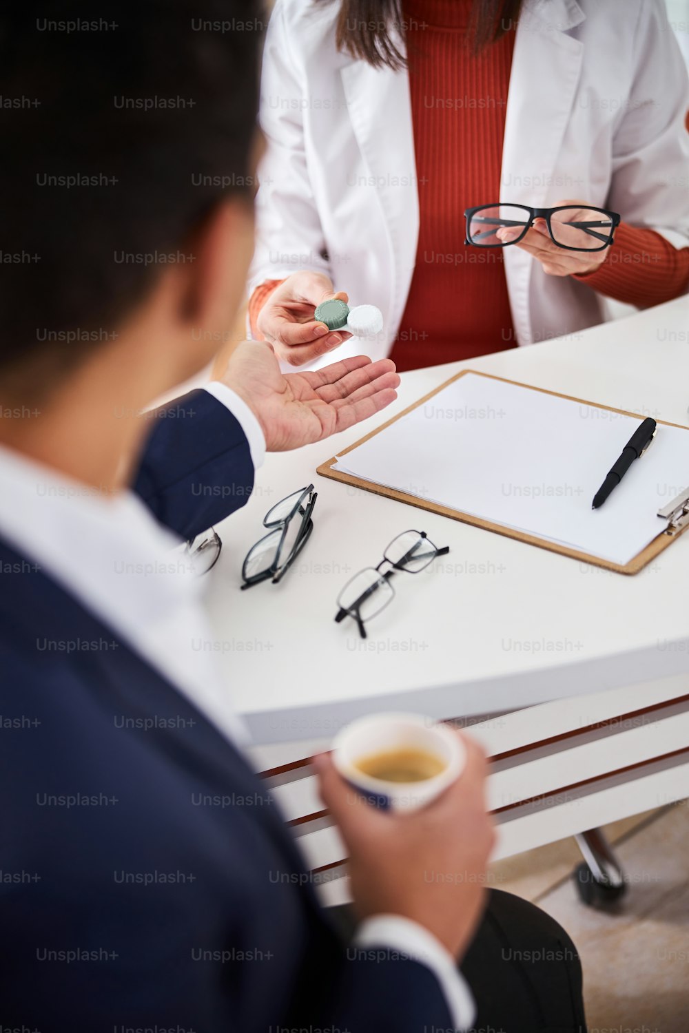 Cropped photo of an optical dispenser offering the eyewear to a customer at the desk