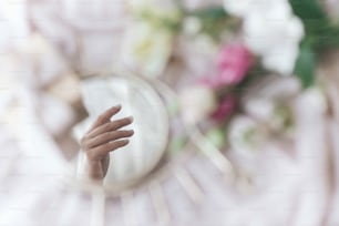 Hand reflected in mirror on background of soft fabric with flowers and gift box. Spring aesthetics. Gentle image. Eye shape boho mirror. Happy Womens and mothers day