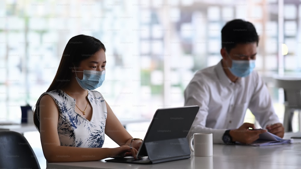 防護マスクを着けた2人のビジネス仲間が、現代のオフィスで新しいプロジェクトに協力しています。
