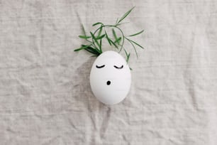 Buona Pasqua! Uovo naturale con faccina addormentata disegnata in graziosa coroncina floreale su tessuto di lino. Concetto di vacanza ecologica a rifiuti zero. Vista dall'alto con spazio per il testo. Cristo è risorto