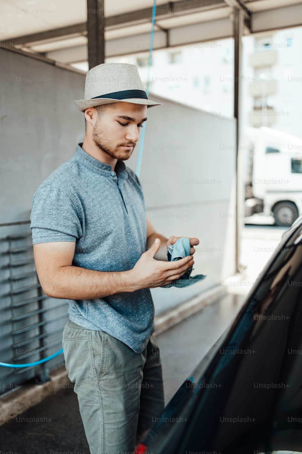 Young handsome man with hat cleaning car with rag, car detailing (or valeting) concept.