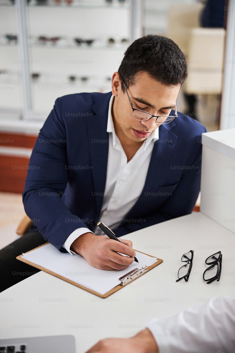 Ernster Mann mit einem Stift in der Hand, der sich über ein leeres Blatt Papier im Büro des Optikers beugt