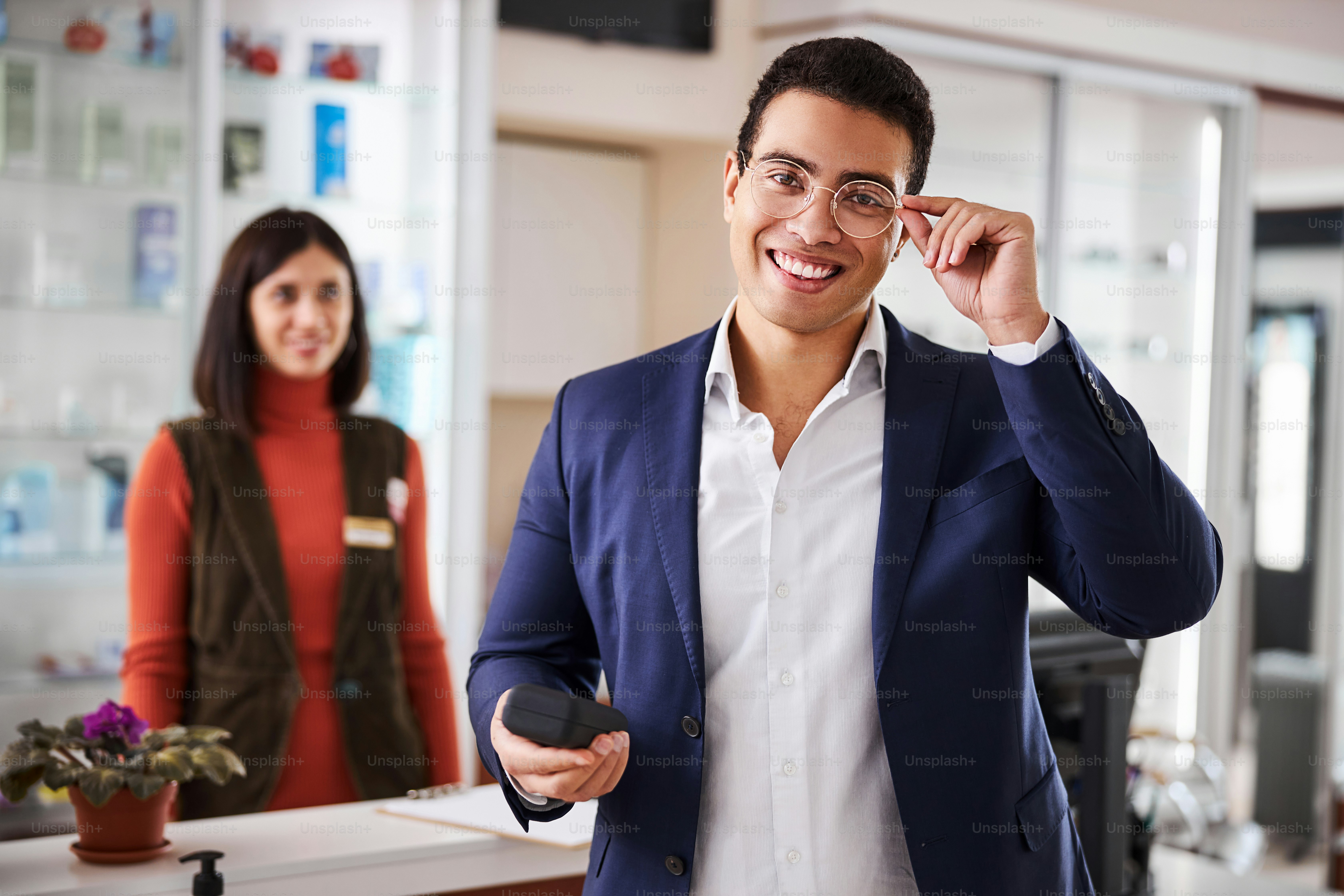 Contented attractive young dark-haired male customer trying on his prescription eyewear at the optician office
