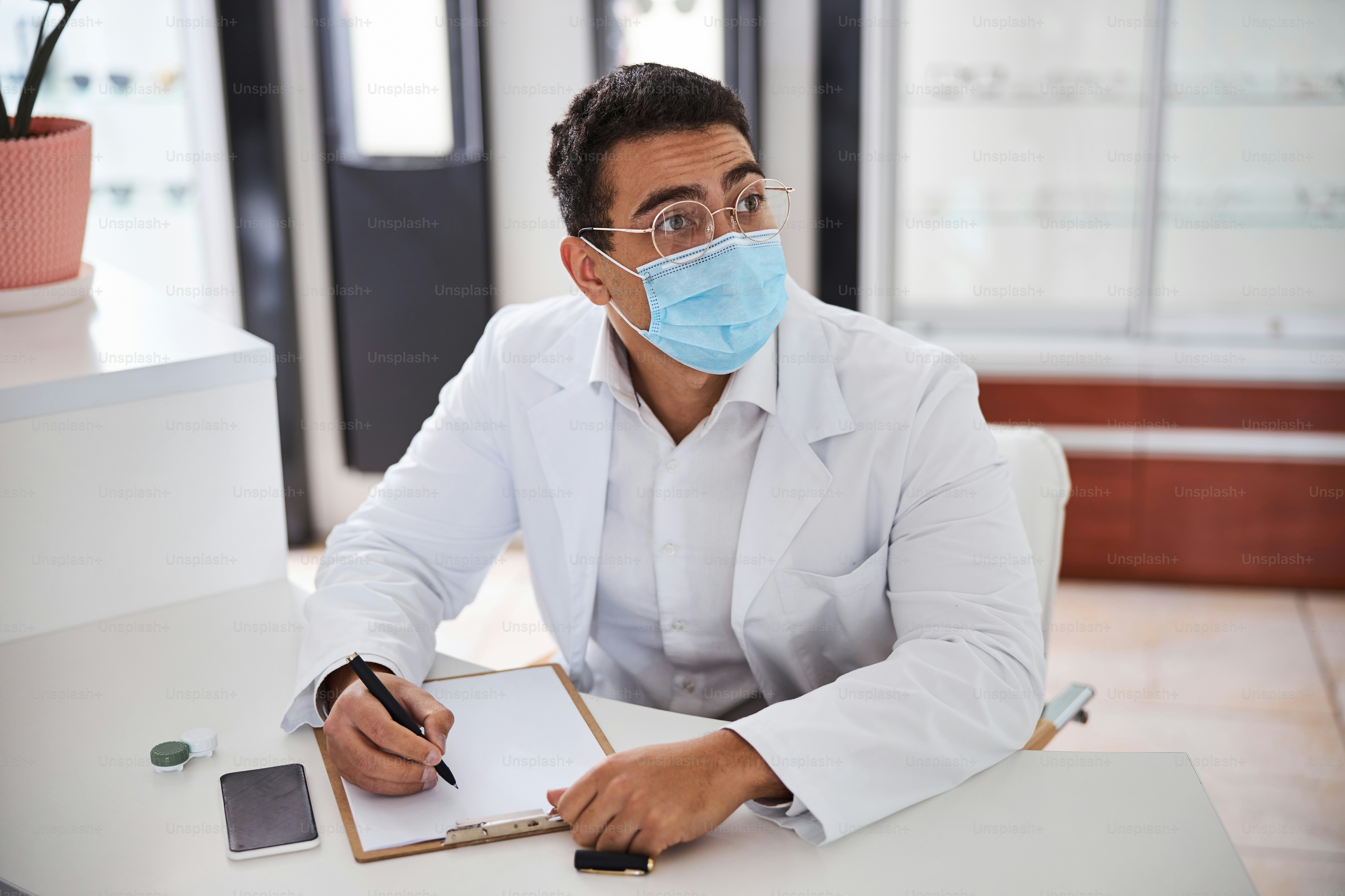 Thoughtful darkhaired male ophthalmologist in a face mask and a lab