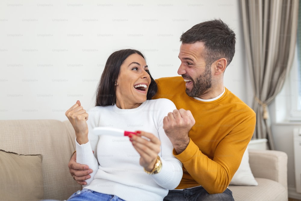 Aufnahme eines glücklichen jungen Paares, das zu Hause einen Schwangerschaftstest macht. Eine glückliche aufgeregte Frau, die einen positiven Schwangerschaftstest macht und feiert. Aufgeregte Frau, die schwanger wird. Paar feiert positives Schwangerschaftstestergebnis zu Hause