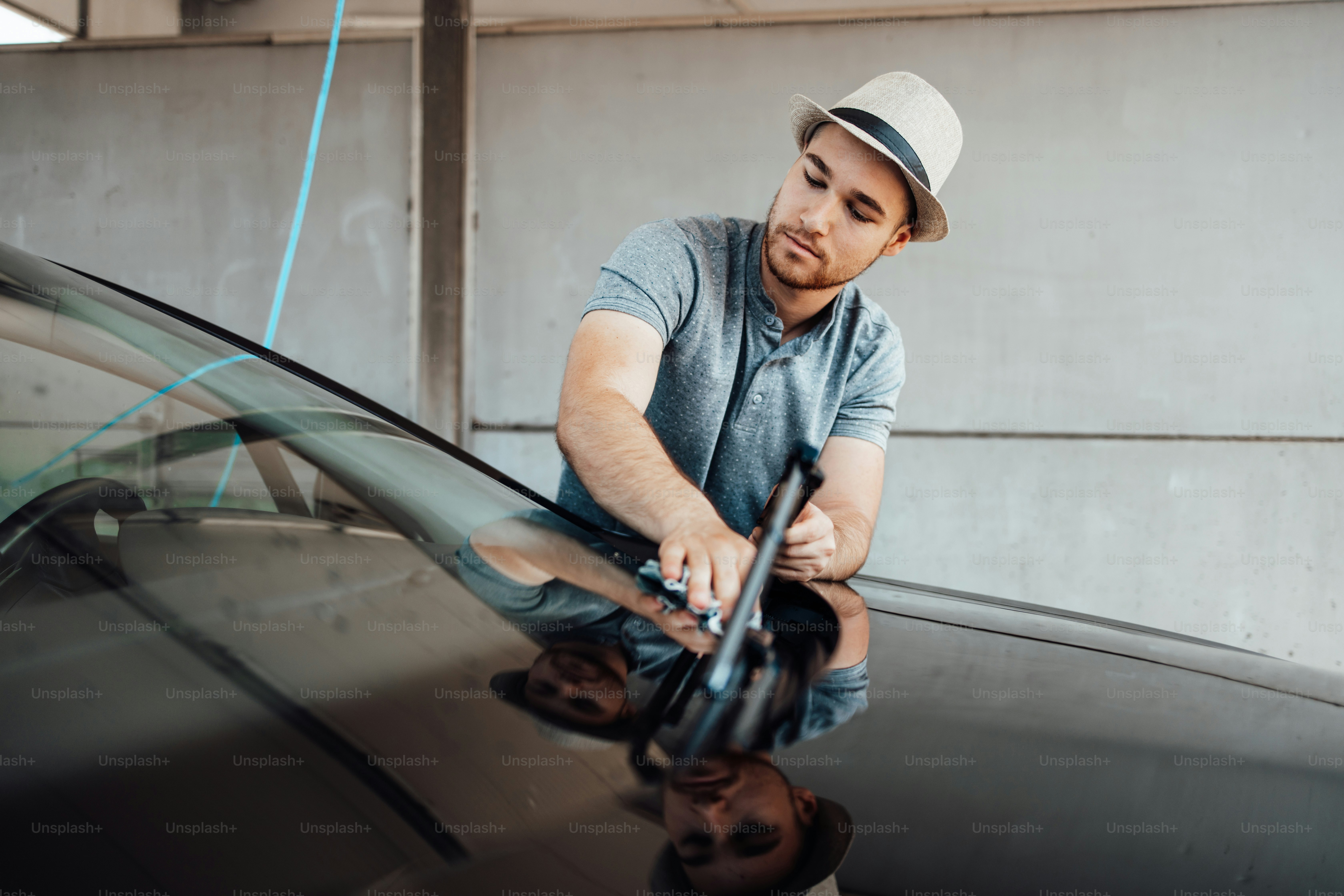 Young handsome man with hat cleaning car with rag, car detailing (or valeting) concept.