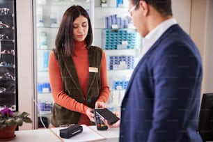 Dark-haired saleswoman holding a POS machine in front of a male customer with a smartphone