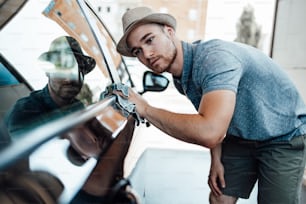 Jeune bel homme avec chapeau de nettoyage de voiture avec chiffon, concept d’esthétique automobile (ou de voiturier).