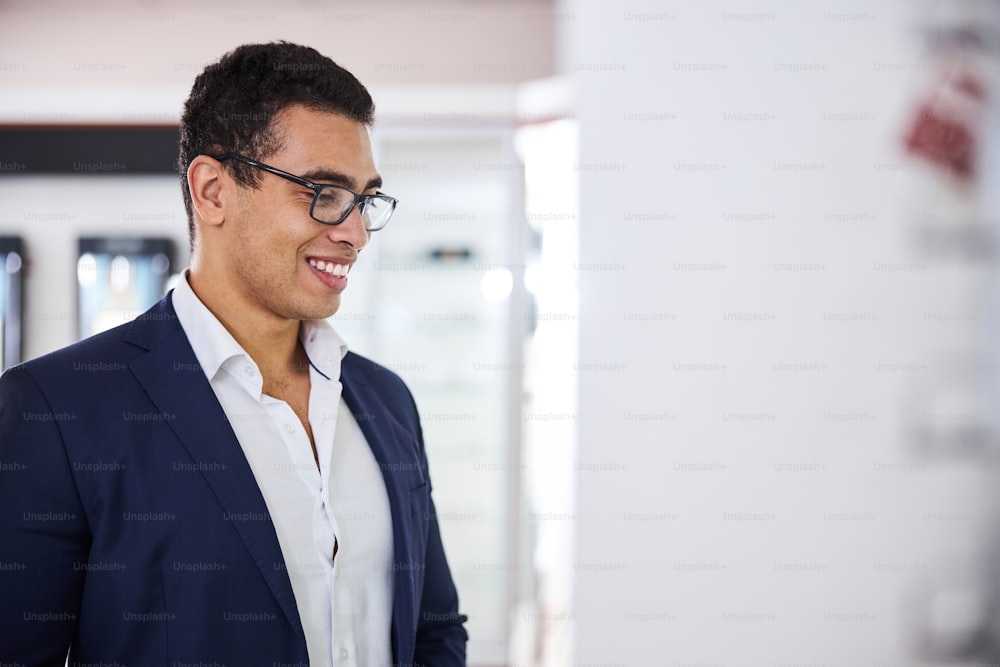 Portrait of a handsome smiling cheerful Latin American dark-haired young male customer wearing fashionable spectacles