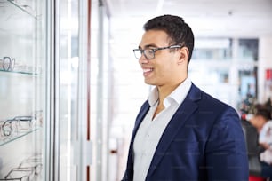Portrait of a smiling young male buyer looking at glasses on the optical display rack