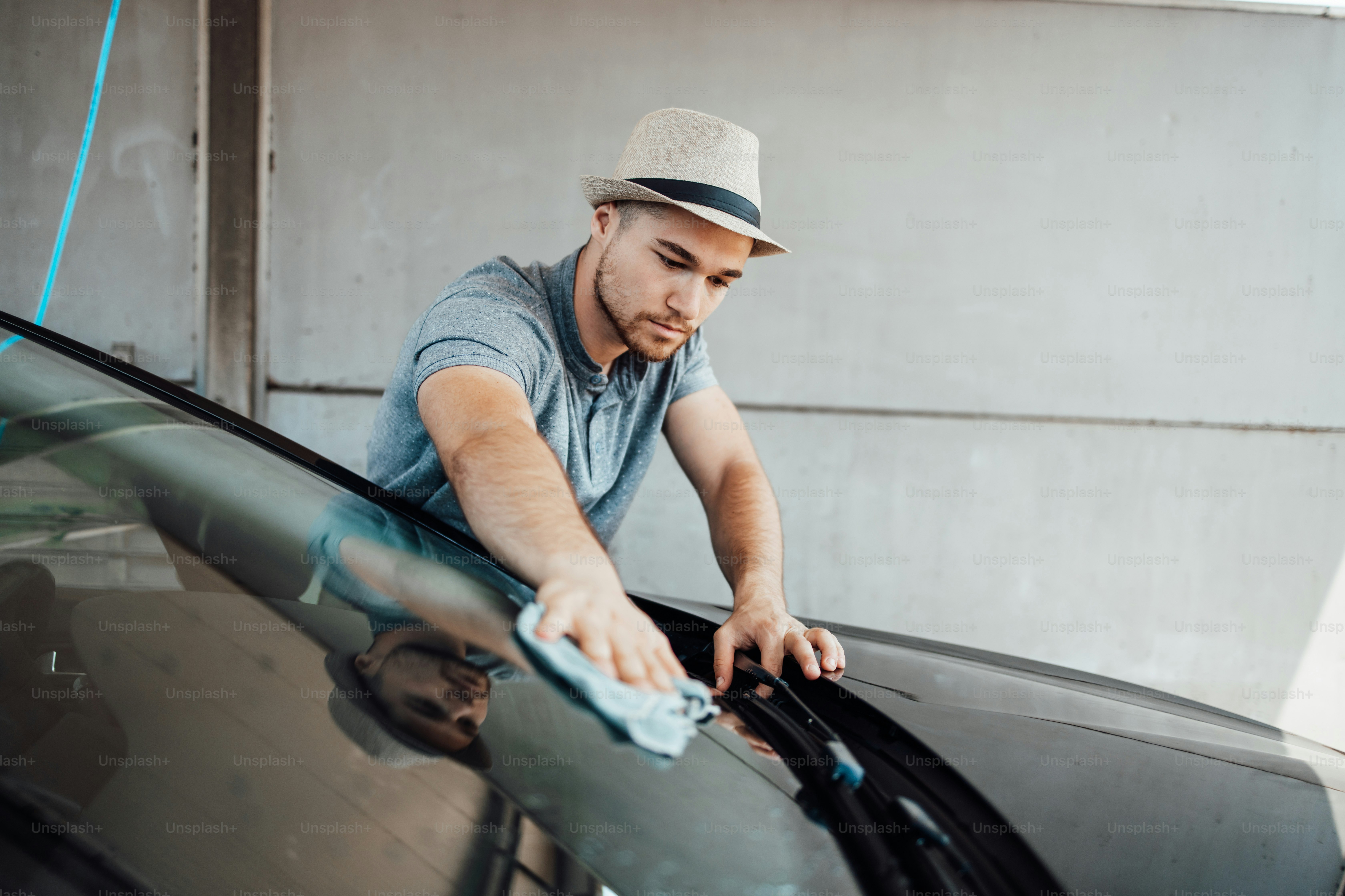 Young handsome man with hat cleaning car with rag, car detailing (or valeting) concept.