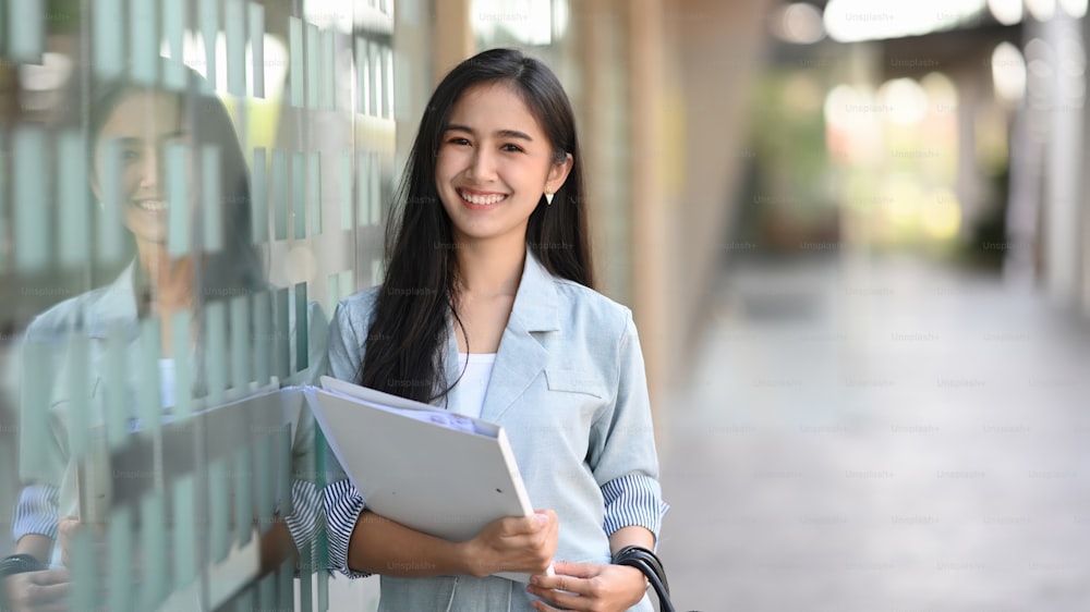 Happy young asian businesswoman holding file and standing outside of office.
