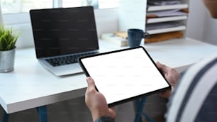 Close up view of young man freelance working with laptop and using digital tablet at home office.