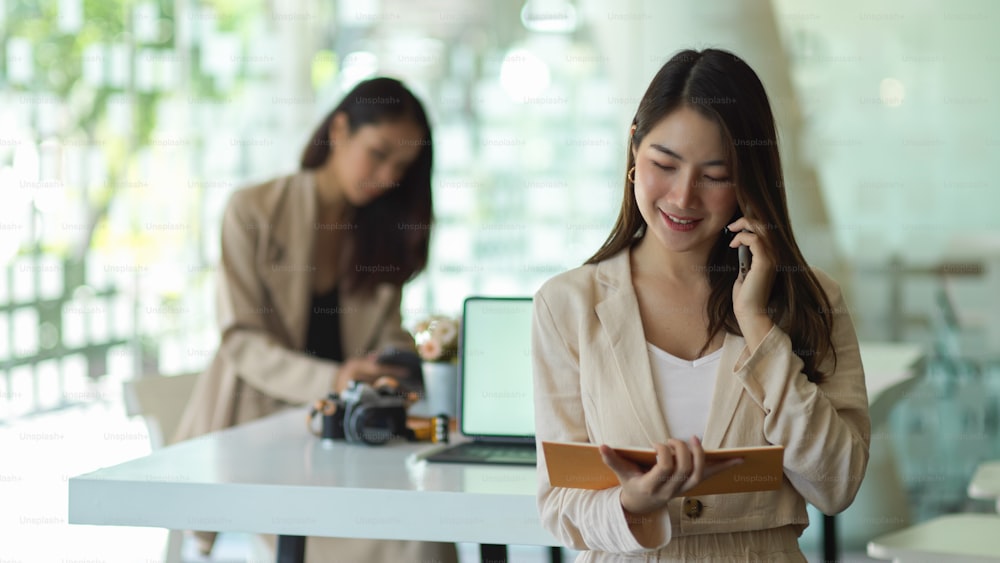 Portrait of businesswoman talking on the phone and reading information on schedule book in office room