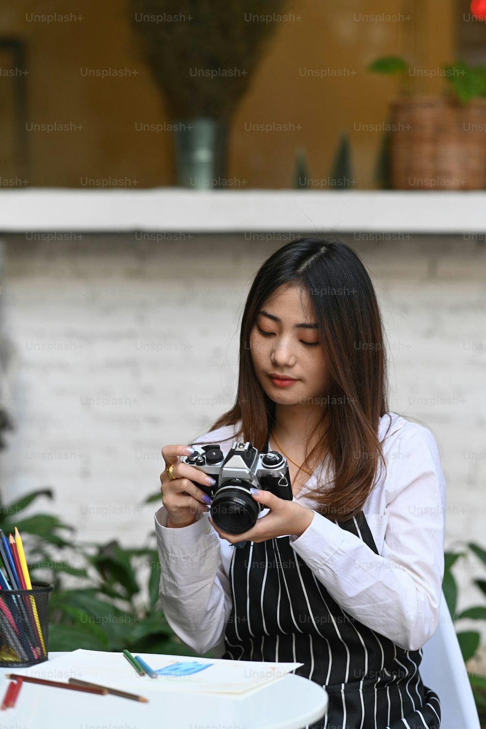 Retrato de uma jovem artista ou fotógrafa verificando a foto na câmera enquanto estava sentada em sua oficina.
